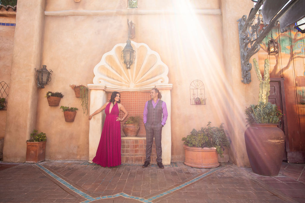 Engaged Couple, Man & Woman in formal attire, interacting at Disneyland posed near fountain in area with Hacienda Spanish Colonial Architecture